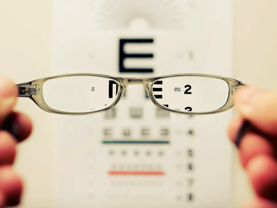Mãos seguram uma armação diante de uma tabela de letras, que fica nítida pela lente
